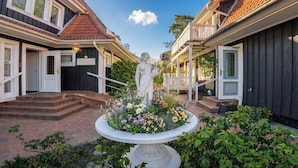 A courtyard with a statue, a flower bed, and a building with a porch.