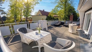 An outdoor patio with a table and chairs, a small table with a vase, and a sofa.