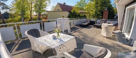 An outdoor patio with a table and chairs, a small table with a vase, and a sofa.