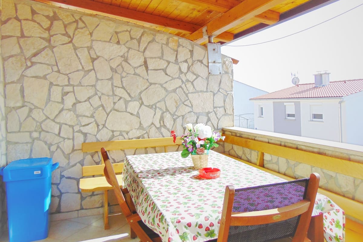 A balcony with a stone wall, wooden ceiling, and a table with a fruit pattern tablecloth.