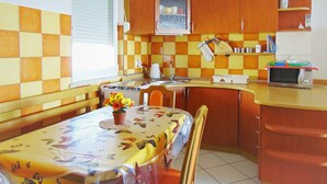 A compact kitchen with wooden cabinets, a microwave, and a dining table with a floral tablecloth. - Segundo al Mar Apartments (Medulin)