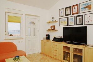 Olohuoneessa on sohva, televisio, kaappi ja ikkuna, josta avautuu näkymä merelle.
