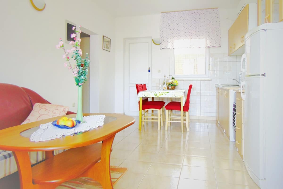 A compact kitchen with a dining area, a refrigerator, and a window with curtains.