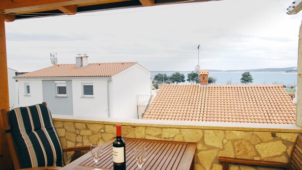 A terrace with a table, a bottle of wine, and a glass. The terrace overlooks a body of water and houses with red-tiled roofs. - Segundo al Mar Apartments (Medulin)