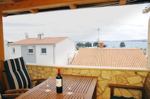 A terrace with a table, a bottle of wine, and a glass. The terrace overlooks a body of water and houses with red-tiled roofs. - Segundo al Mar Apartments (Medulin)