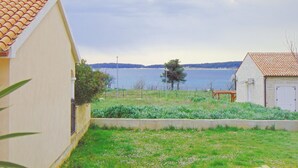 A residential area with a house featuring a tiled roof, a small garden, and a view of a body of water in the background. - Segundo al Mar Apartments (Medulin)