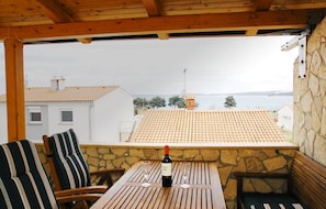 A wooden table with a bottle of wine and two glasses, set against a stone wall with a view of a town and water. - Segundo al Mar Apartments (Medulin)