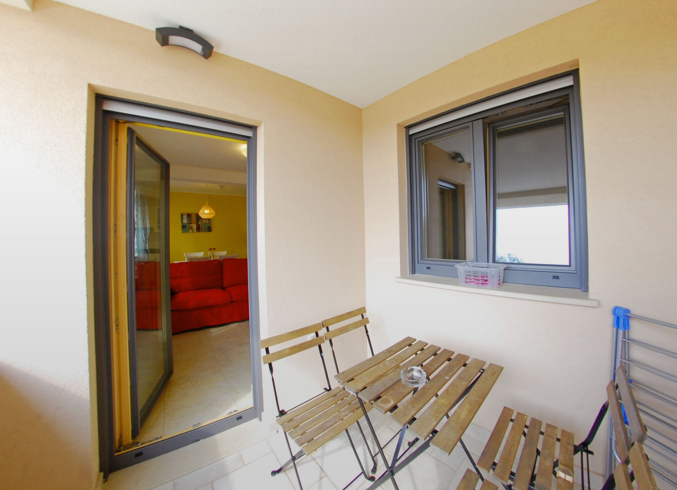 A room with a wooden bench, a window, and a door leading to another room with a red sofa.
