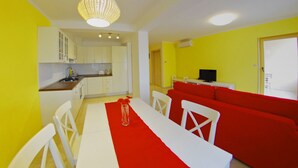 Une cuisine moderne avec des meubles blancs, une table à manger agrémentée d’un chemin de table rouge et un canapé rouge dans une pièce jaune.