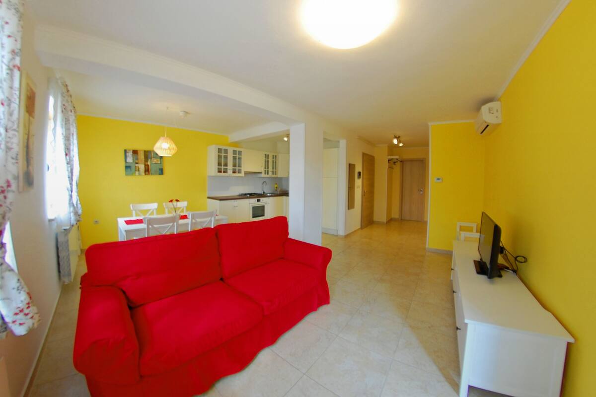 Un salon avec un canapé rouge, un meuble TV blanc et un mur jaune.