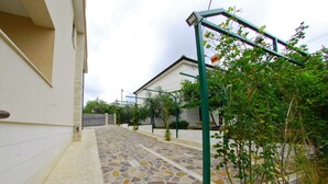 Un chemin pavé mène à une maison dont l’entrée est recouverte de pierres et qui est dotée d’un portail en métal vert.