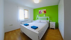 Une chambre à coucher avec un lit, des tables de chevet, un radiateur, une fenêtre avec des rideaux et un mur vert.