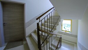 Un escalier avec une main courante en bois et des balustres en métal, menant à un palier doté d’une porte et d’une fenêtre offrant une vue sur la verdure.