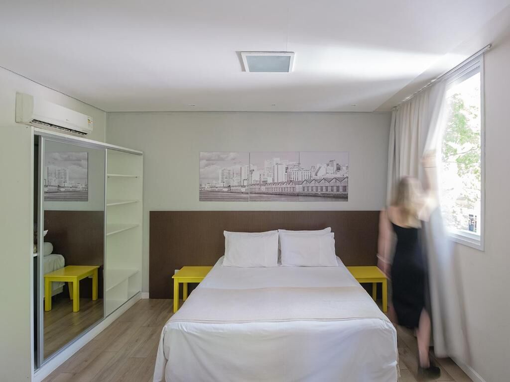Hotelkamer met een bed, een stadsgezichtschilderij aan de muur, een kledingkast en een raam met gordijnen.