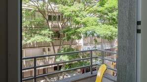 A view from a window overlooking a building with a balcony and a tree. - Açores Flat Design (Porto Alegre)