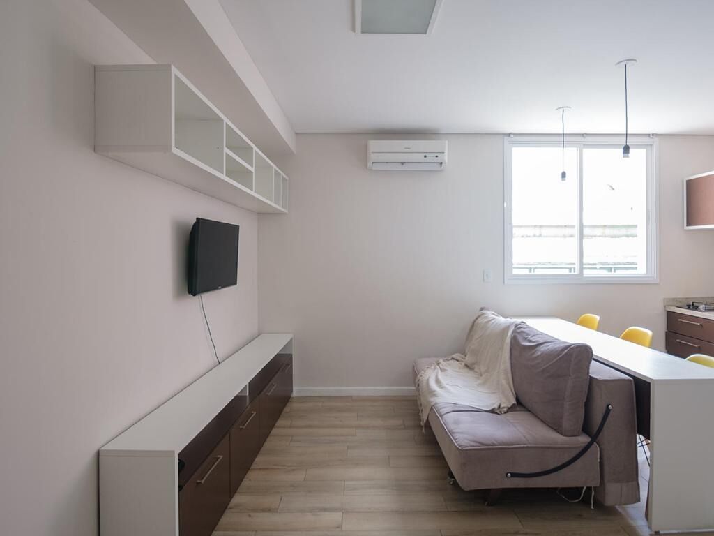 Un salon moderne avec un canapé, un téléviseur à écran plat fixé au mur, un banc intégré et une fenêtre laissant entrer la lumière naturelle.