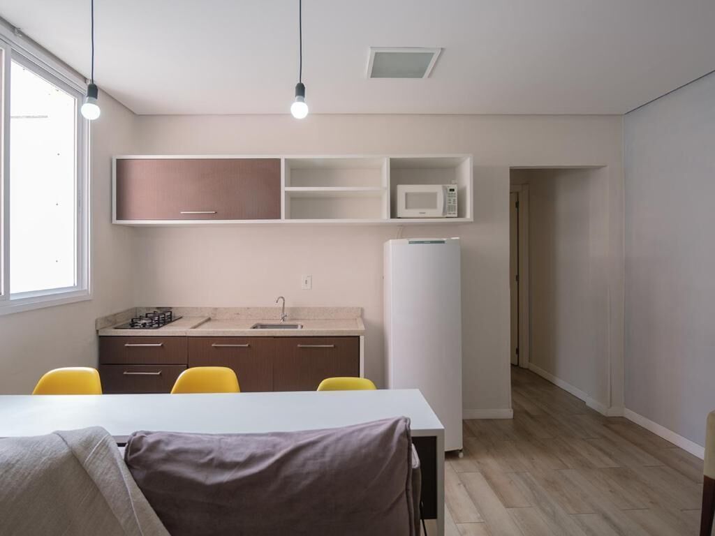 A modern kitchen with a microwave, refrigerator, and a sink. There is a dining table with chairs and a window providing natural light.