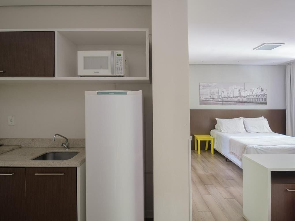 Een compacte hotelkamer met kitchenette, een bed en een klein tafeltje.
