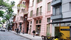 A street with pink buildings, a café with outdoor seating, and a shop with a yellow shutter. - Açores Flat Design (Porto Alegre)