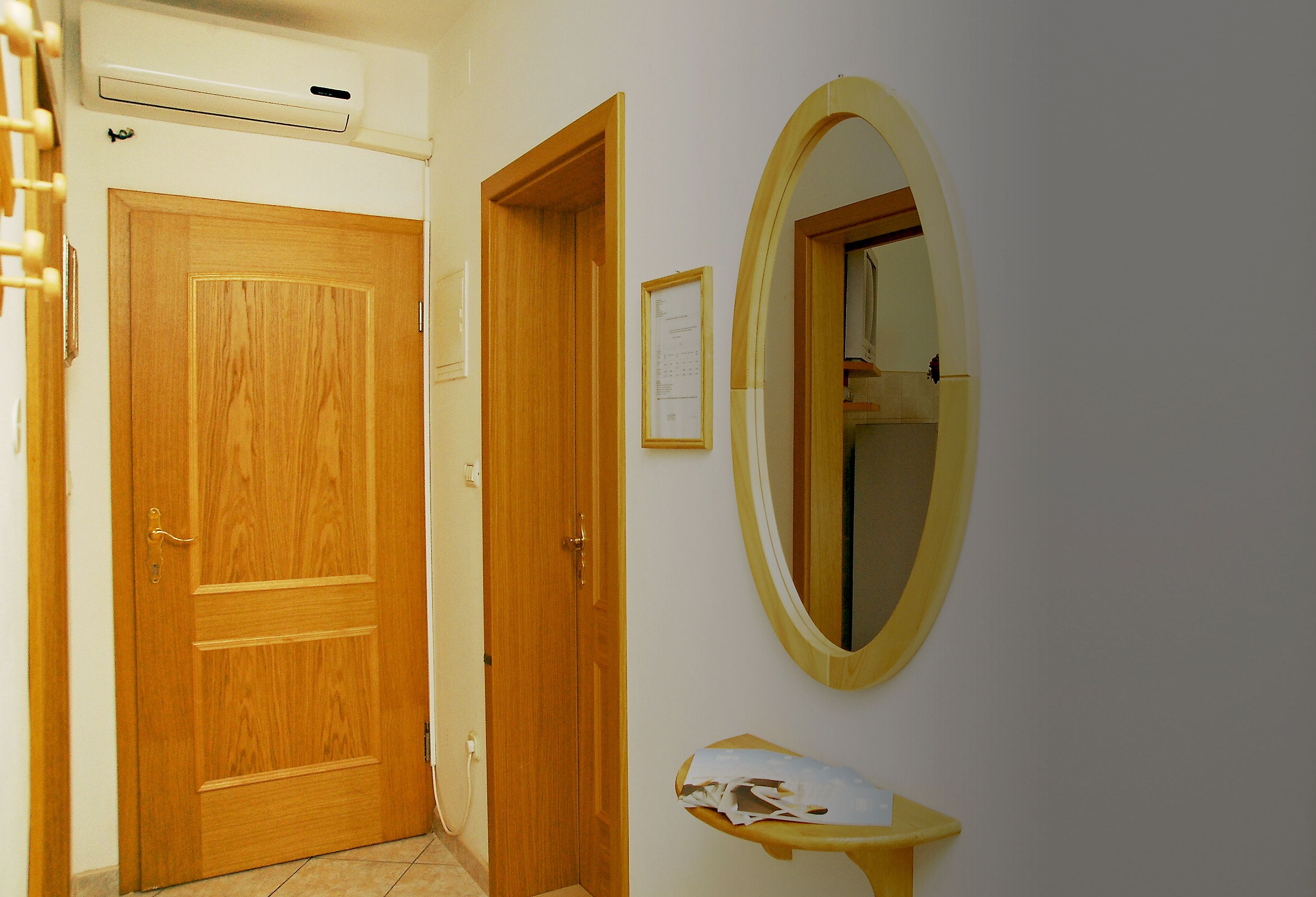A hallway with a wooden door, a framed notice, and a mirror on the wall.
