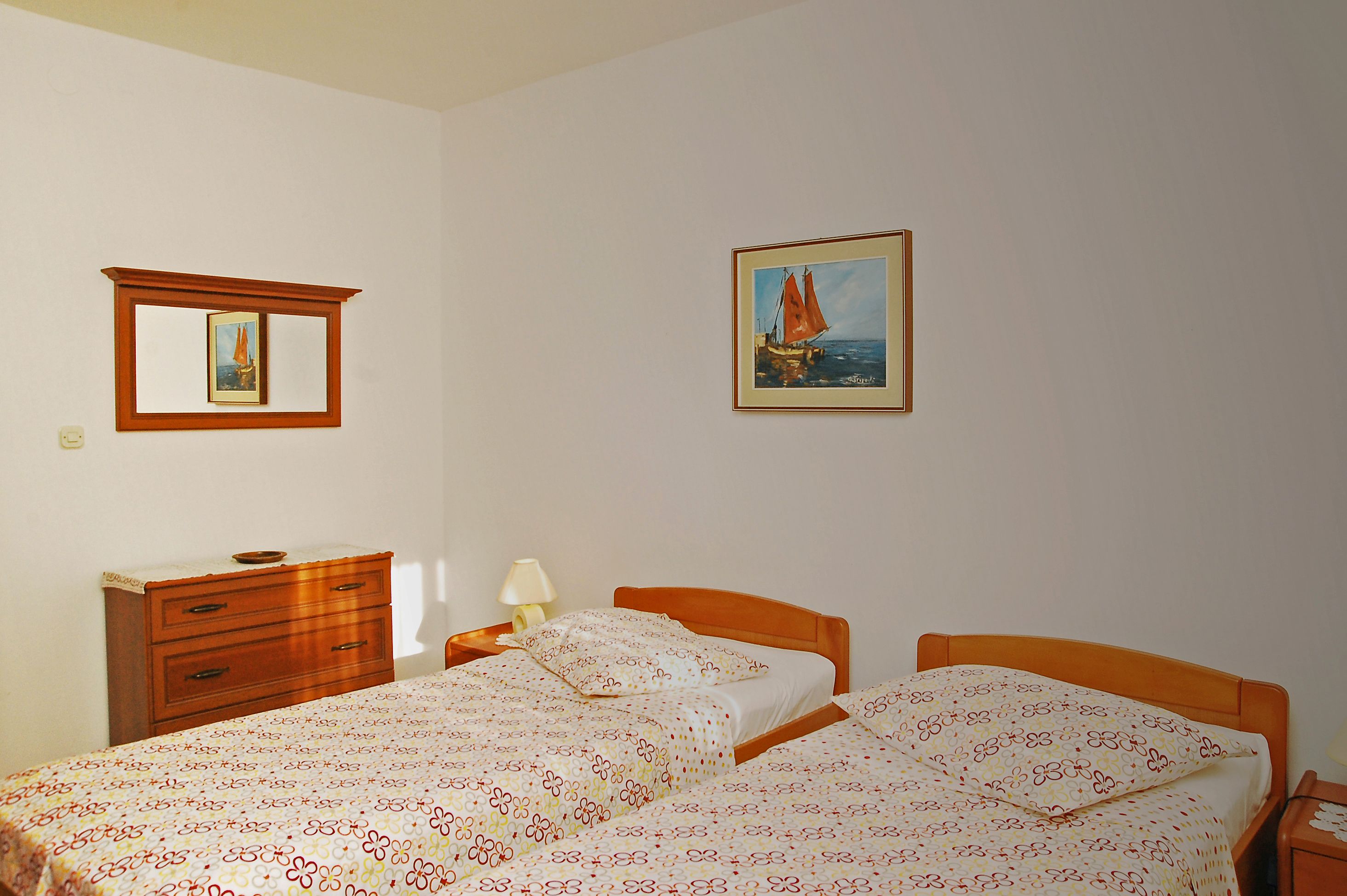 A bedroom with a bed, a nightstand, a dresser, a mirror, and a painting of a sailboat.