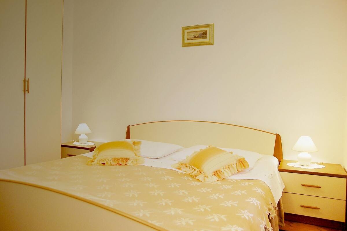 A neatly made bed with a floral bedspread, two bedside lamps, and a small picture frame on the wall.