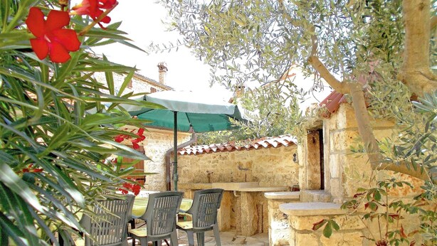 An outdoor patio with stone walls, a table with chairs, and potted plants. - Sol Jardin Apartments (Medulin)