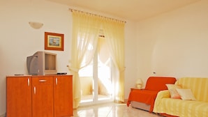 A room with a wooden cabinet, a television, a sofa, and a sliding glass door leading to a balcony. - Sol Jardin Apartments (Medulin)