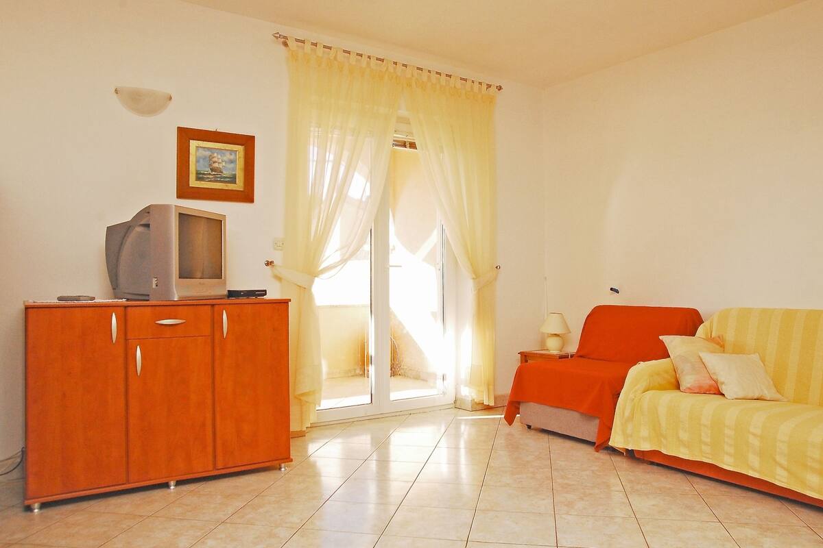 A room with a wooden cabinet, a television, a sofa, and a sliding glass door leading to a balcony.