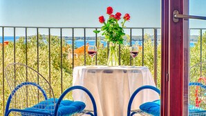 A balcony with a table set for two, featuring a vase with red flowers and two wine glasses. - Blue Story Apartments (Fazana)