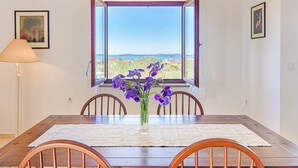 A dining table with chairs, a vase with purple flowers, and a view of the sea through an open window. - Blue Story Apartments (Fazana)