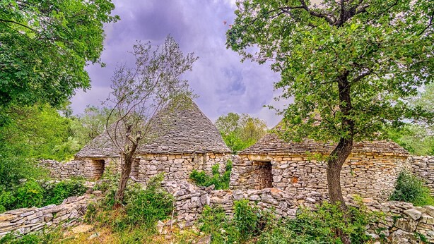 A stone building with a conical roof, surrounded by lush greenery and trees. - Blue Story Apartments (Fazana)