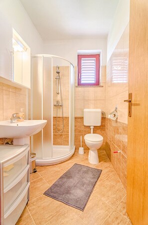 A bathroom with a shower, toilet, sink, and a small window. - Blue Story Apartments (Fazana)