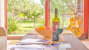A room with a large window, a guitar, a bottle of wine, a bowl of fruit, and some magazines on a table. - Blue Story Apartments (Fazana)