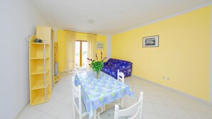 A dining area with a table, chairs, a bookshelf, and a sofa. - Storia di Mare Apartments (Rasa)
