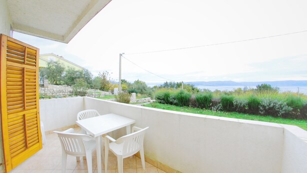 A balcony with a white table and chairs, a yellow shutter, and a view of greenery and a body of water. - Storia di Mare Apartments (Rasa)