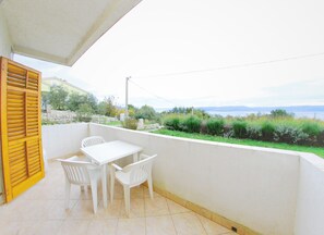 A balcony with a white table and chairs, a yellow shutter, and a view of greenery and a body of water. - Storia di Mare Apartments (Rasa)