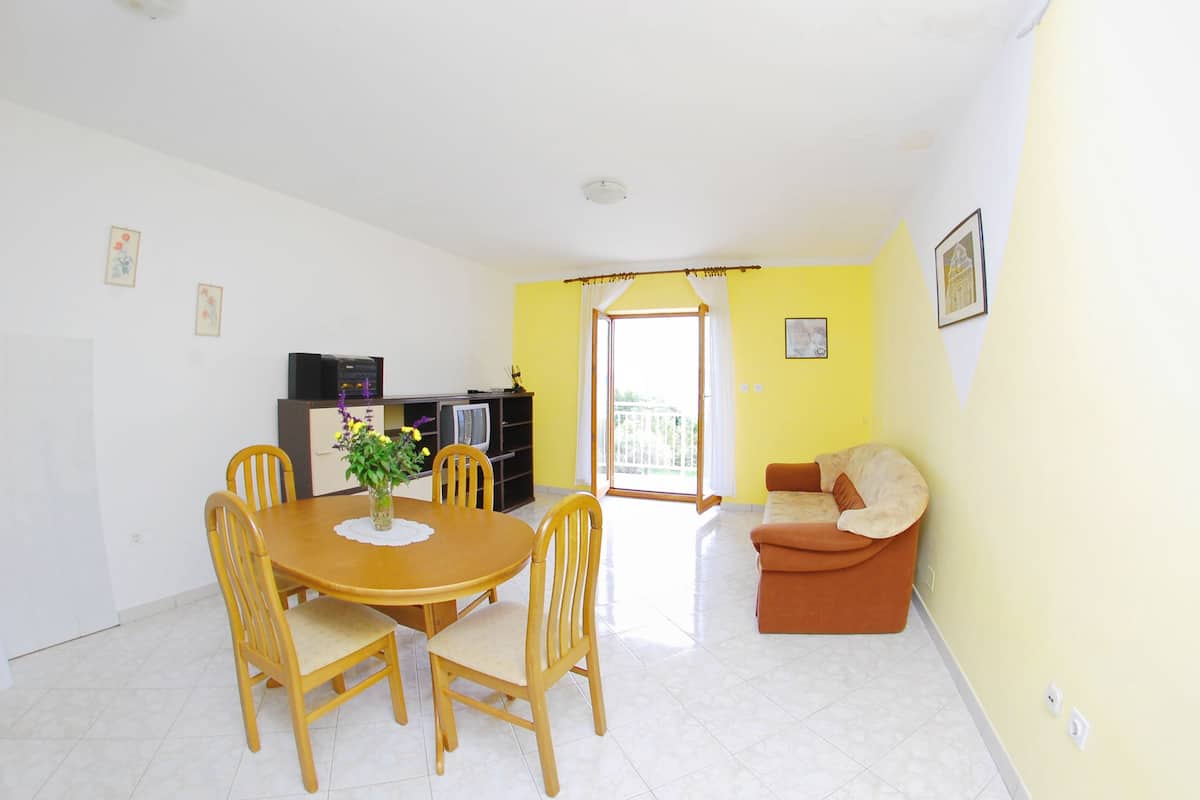 A living room with a dining table and chairs, a sofa, and a kitchen area with appliances.