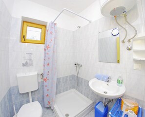 A bathroom with a toilet, sink, shower, and a small window.