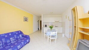 A compact living space with a sofa, a dining table with chairs, a kitchen area, and a television on a stand. - Storia di Mare Apartments (Rasa)