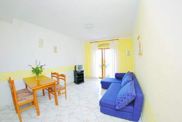 A living room with a blue sofa, wooden dining table, chairs, a TV, and a plant.