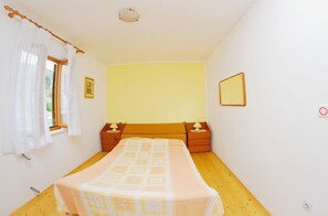 A bedroom with a bed, wooden floor, two bedside tables with lamps, a window with curtains, a wall-mounted mirror, and a light switch.