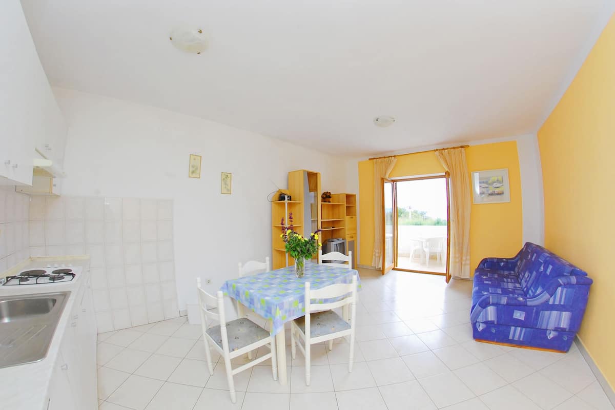 A kitchen with white cabinets, a dining table with a blue tablecloth, and a sofa in a room with yellow walls.