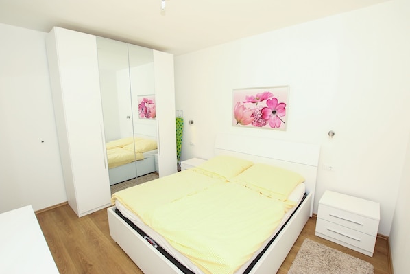 A bedroom with a bed, a wardrobe, a bedside table, and a wall-mounted artwork.