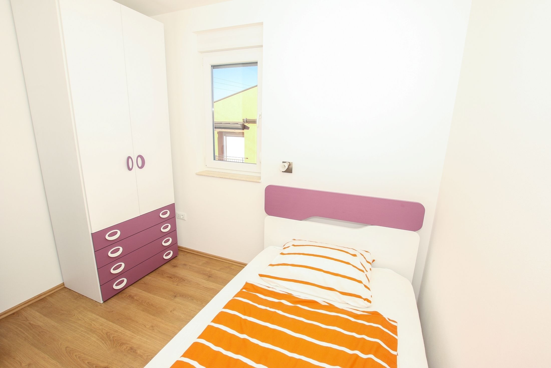 A bedroom with a bed, a wardrobe, a window, and a door.