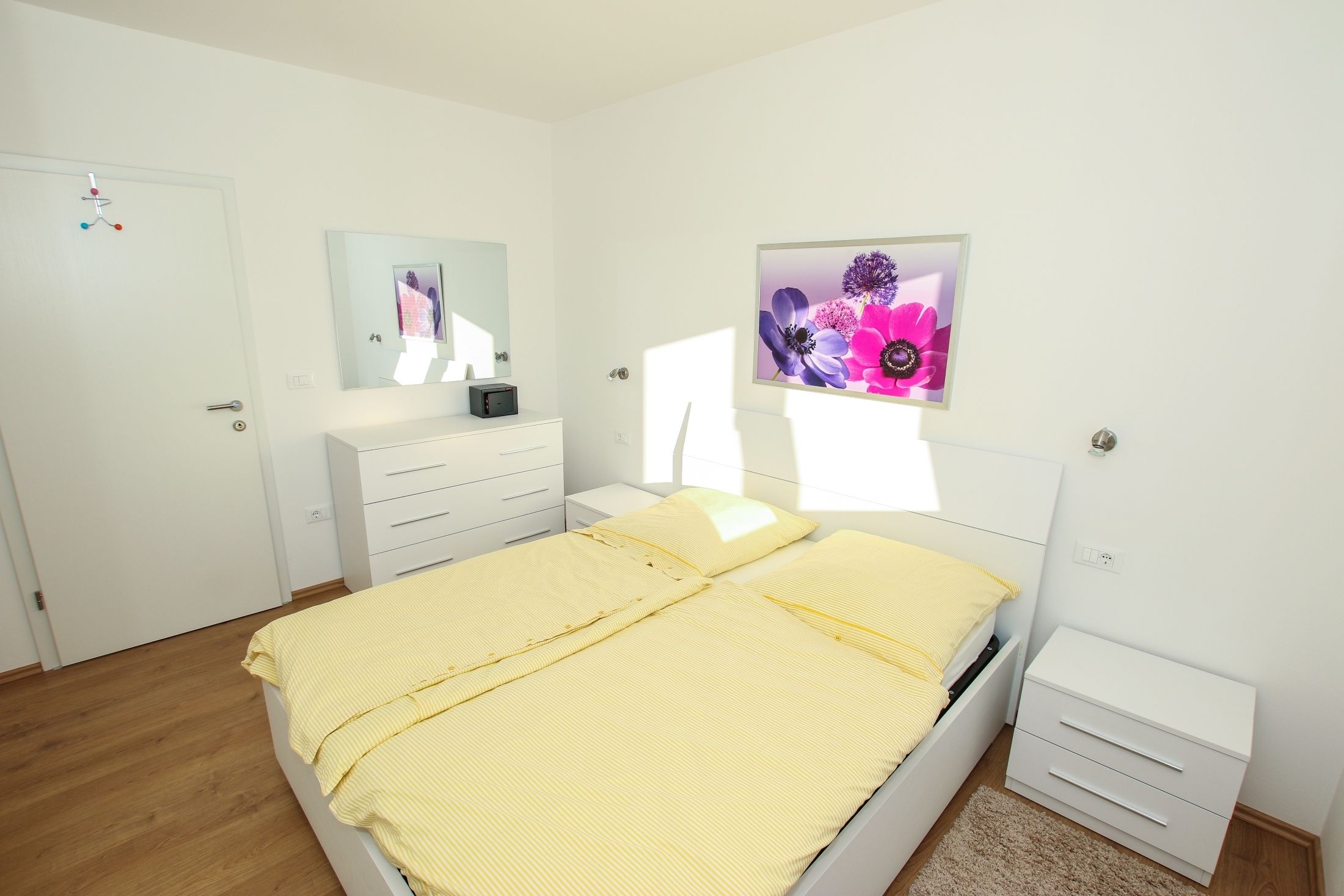A bedroom with a bed, a bedside table, a nightstand, a dresser, a mirror, and a wall-mounted picture.