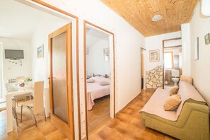 A room with a wooden ceiling, a bed with a pink bedspread, a green sofa with a beige throw, and a dining area with a white table and chairs. - Vacation Pool Apartments (Sveta Nedelja)