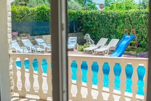 A pool area with lounge chairs and a slide, surrounded by greenery. - Vacation Pool Apartments (Sveta Nedelja)