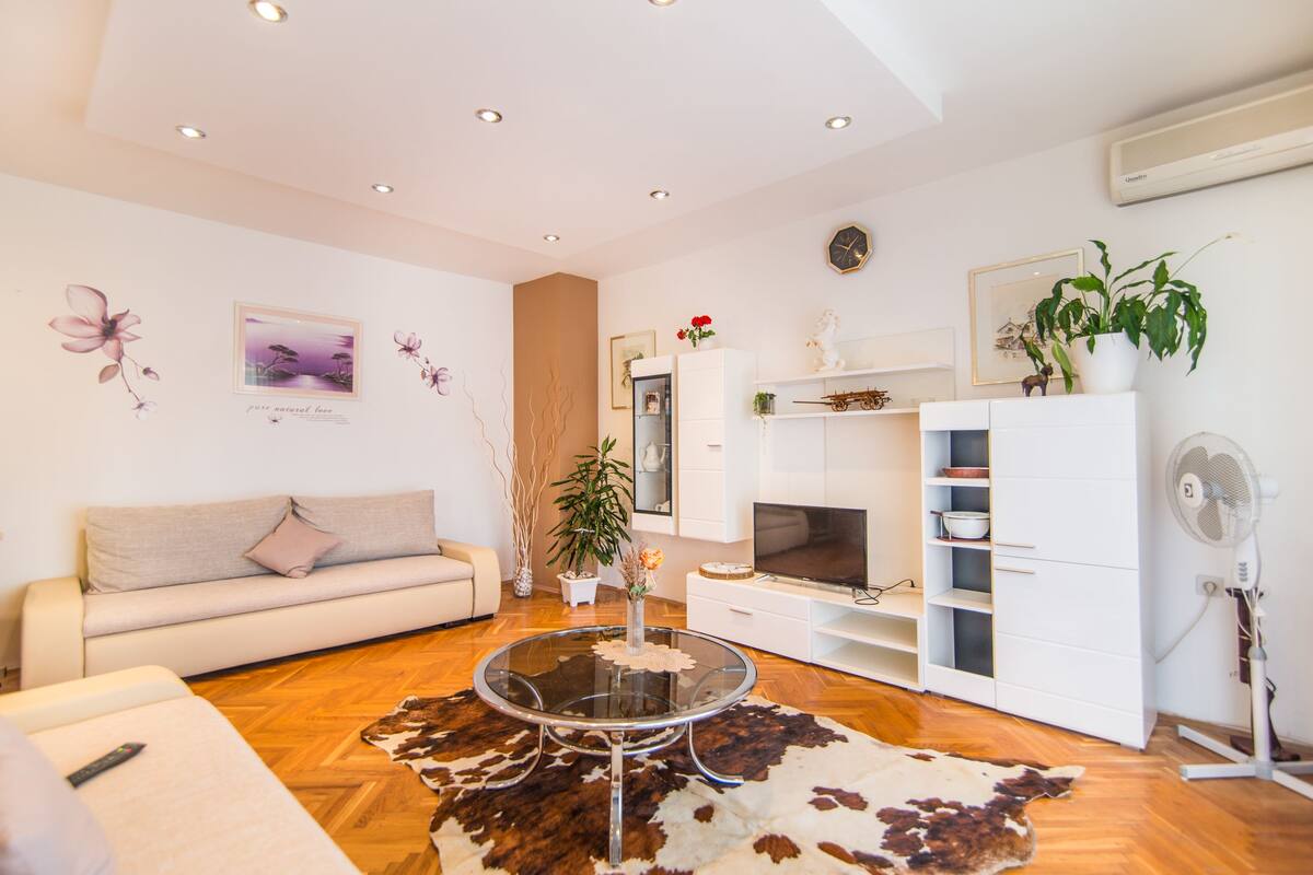 Un salon moderne avec une table basse en verre, un canapé, un téléviseur et un meuble de rangement blanc.
