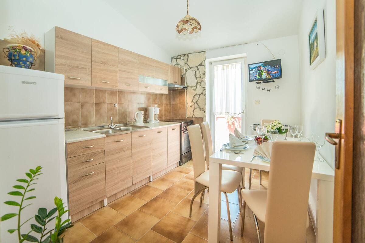 Une cuisine moderne avec des meubles en bois, un réfrigérateur blanc et un coin repas avec une table mise pour deux personnes.